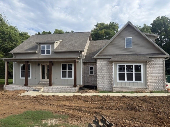Front view of a gray-brick and siding house under construction, with a covered porch and large front windows. (informative)