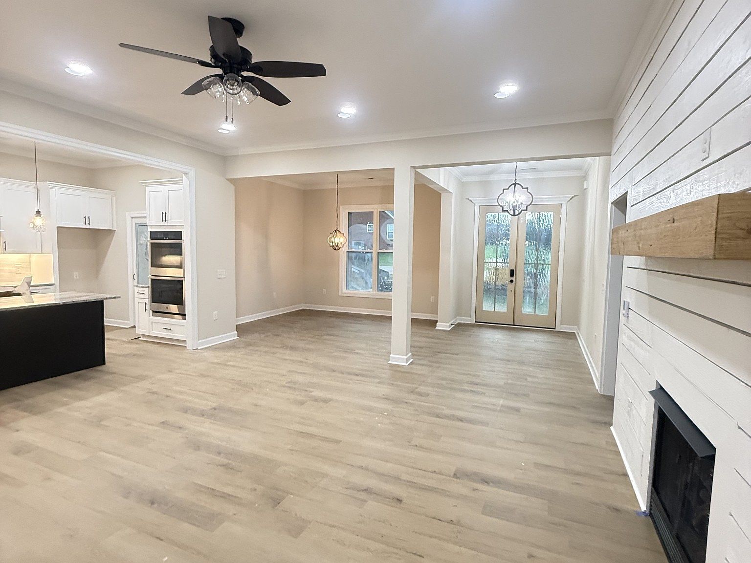 Open-concept living area with white kitchen cabinets, double ovens, and a dark island on light wood flooring.
