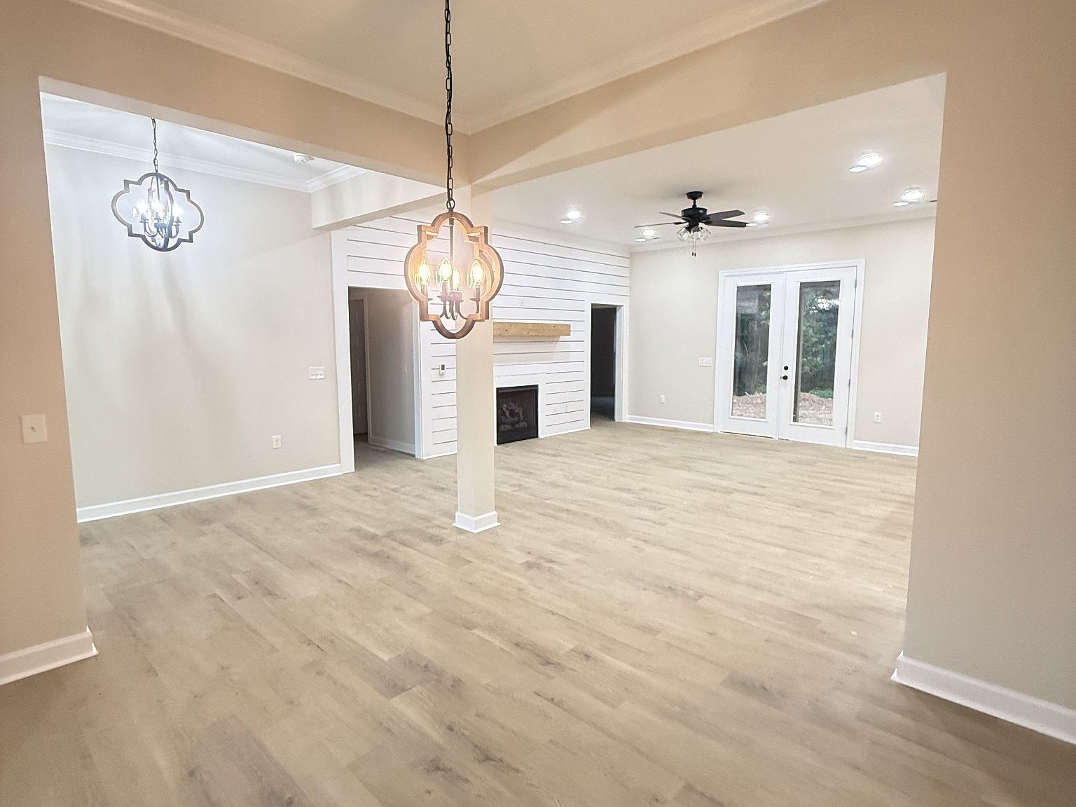 Bright living room with light wood floors, beige walls, a white shiplap fireplace, and French doors to the outdoors.