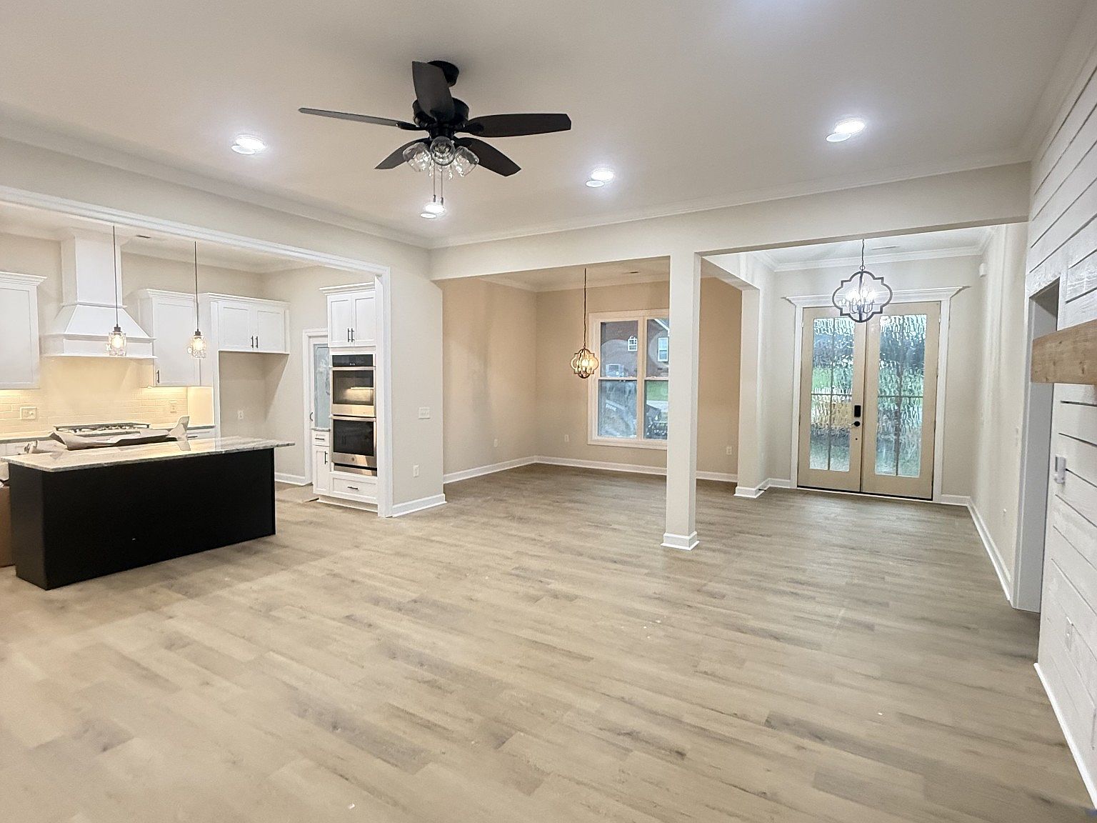 Open-concept kitchen and living area with white cabinets, island, and stainless oven; light wood floors and ceiling fan.