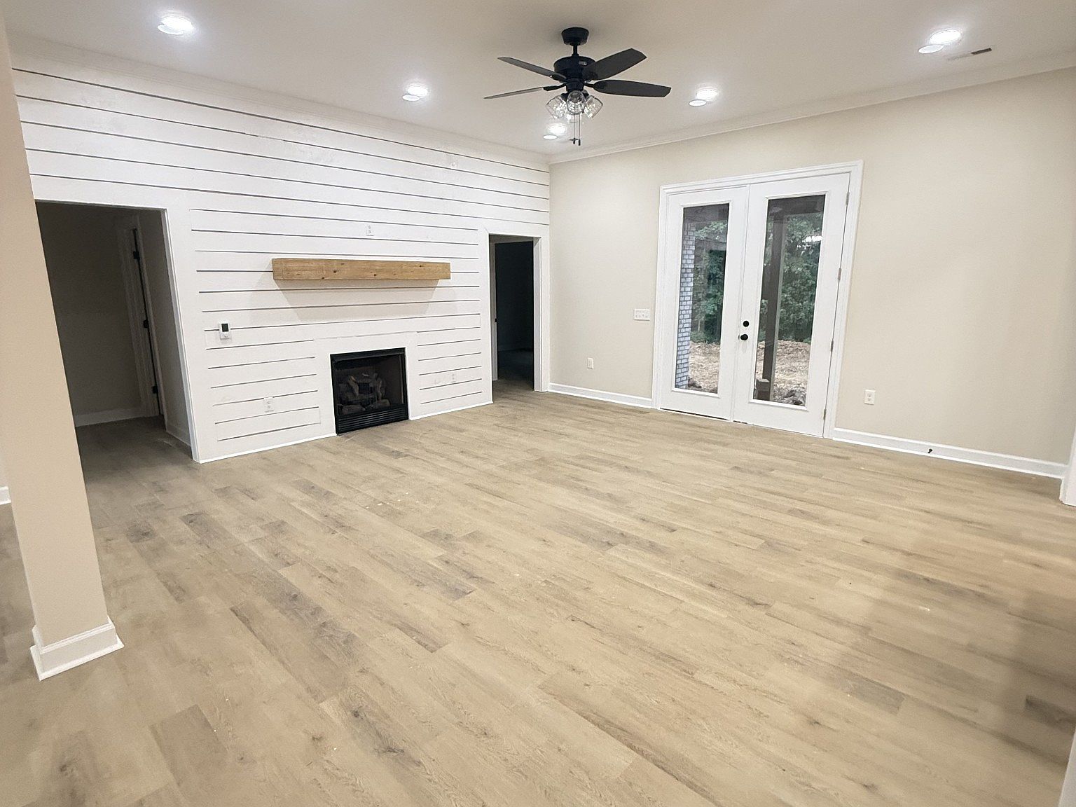 Bright living room with a white shiplap accent wall, a gas fireplace with a wooden mantel, and light hardwood floors.