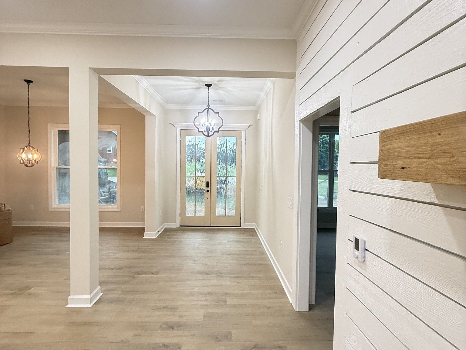 Bright entryway with double glass doors, a chandelier, and light wood flooring in a neutral-toned home interior