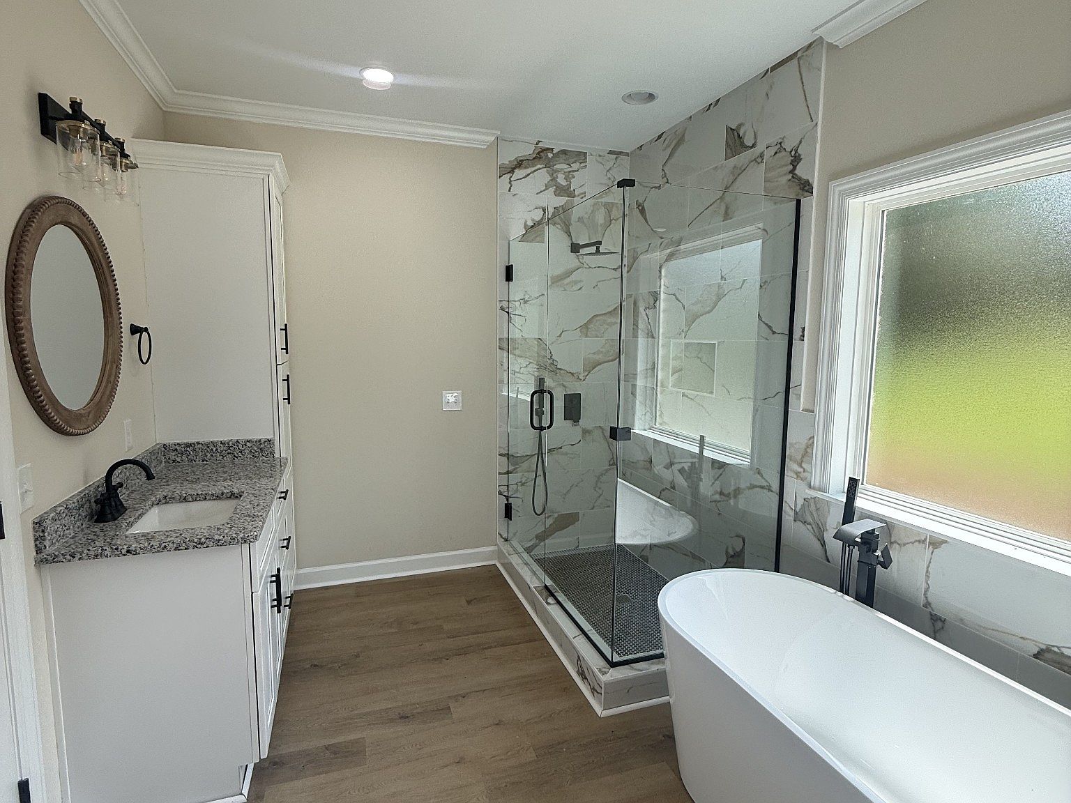 Modern bathroom with white vanity, granite countertop, oval mirror, and black hardware on beige walls.