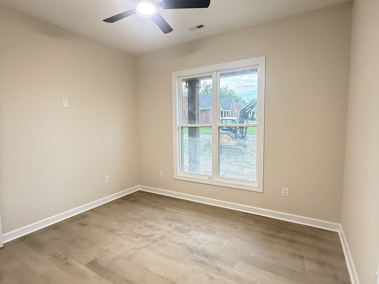 Small empty bedroom with beige walls, light wood floor, and a window; ceiling fan above.