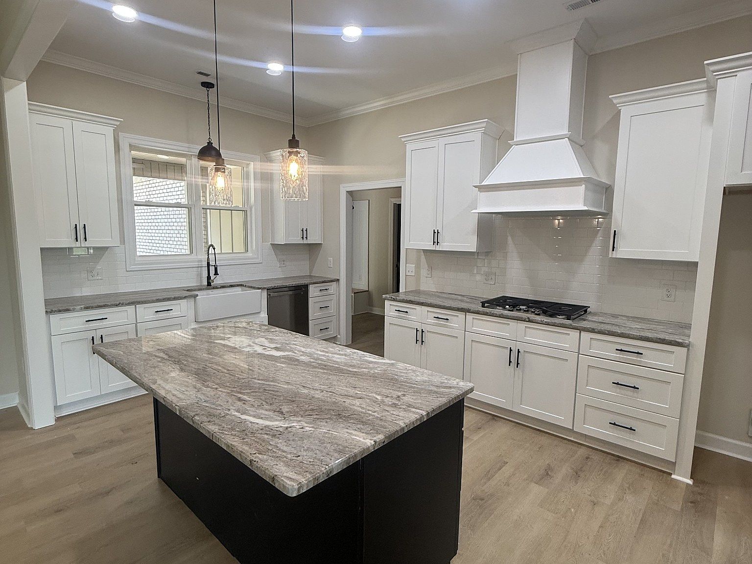 Bright modern kitchen with white cabinets, marble island, and stainless steel appliances visible under a windowed sink area.