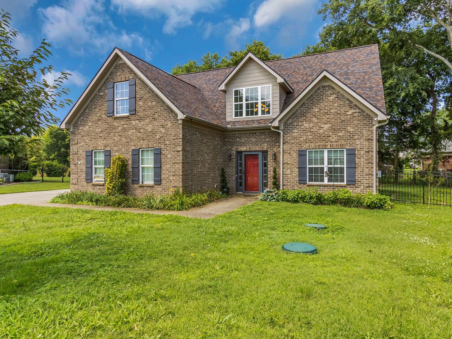 110 Bancroft Ct photo 2 Brick suburban house with red front door and gray shutters, a well-kept lawn, and a dormer window above the entryway.