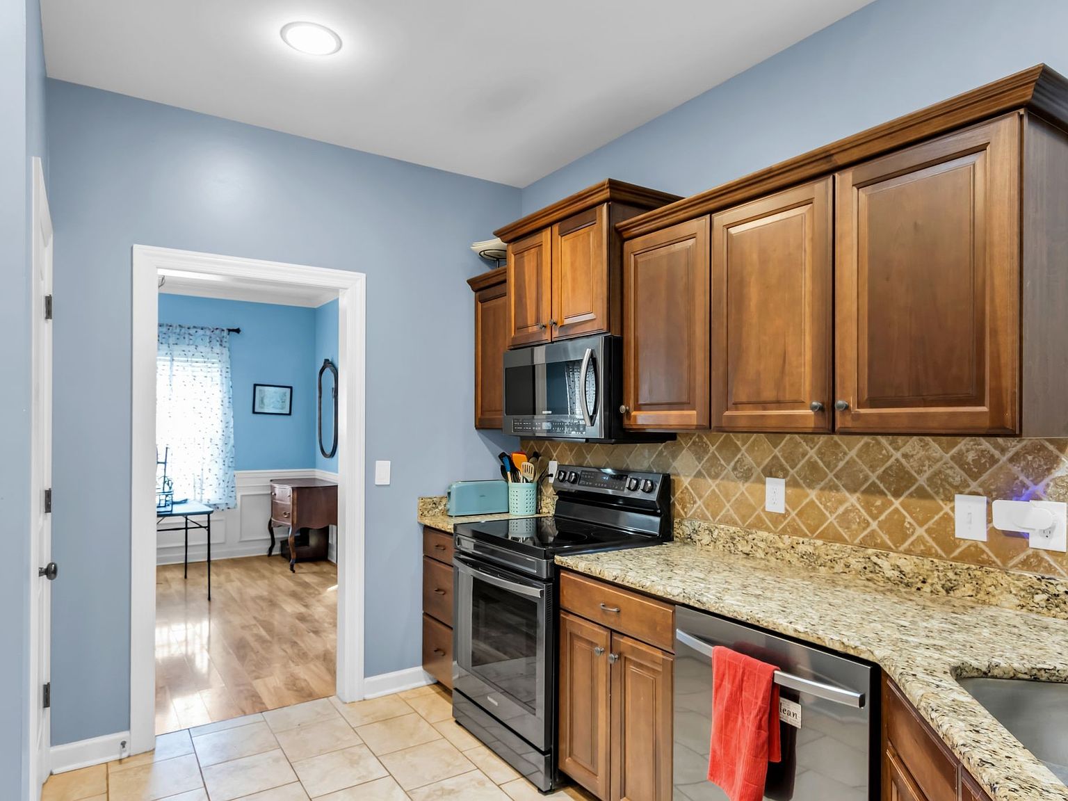 110 Bancroft Ct photo 9 Blue-walled kitchen with granite countertops, dark wood cabinets, and stainless steel oven and microwave; doorway leads to a blue-adorned adjacent room.