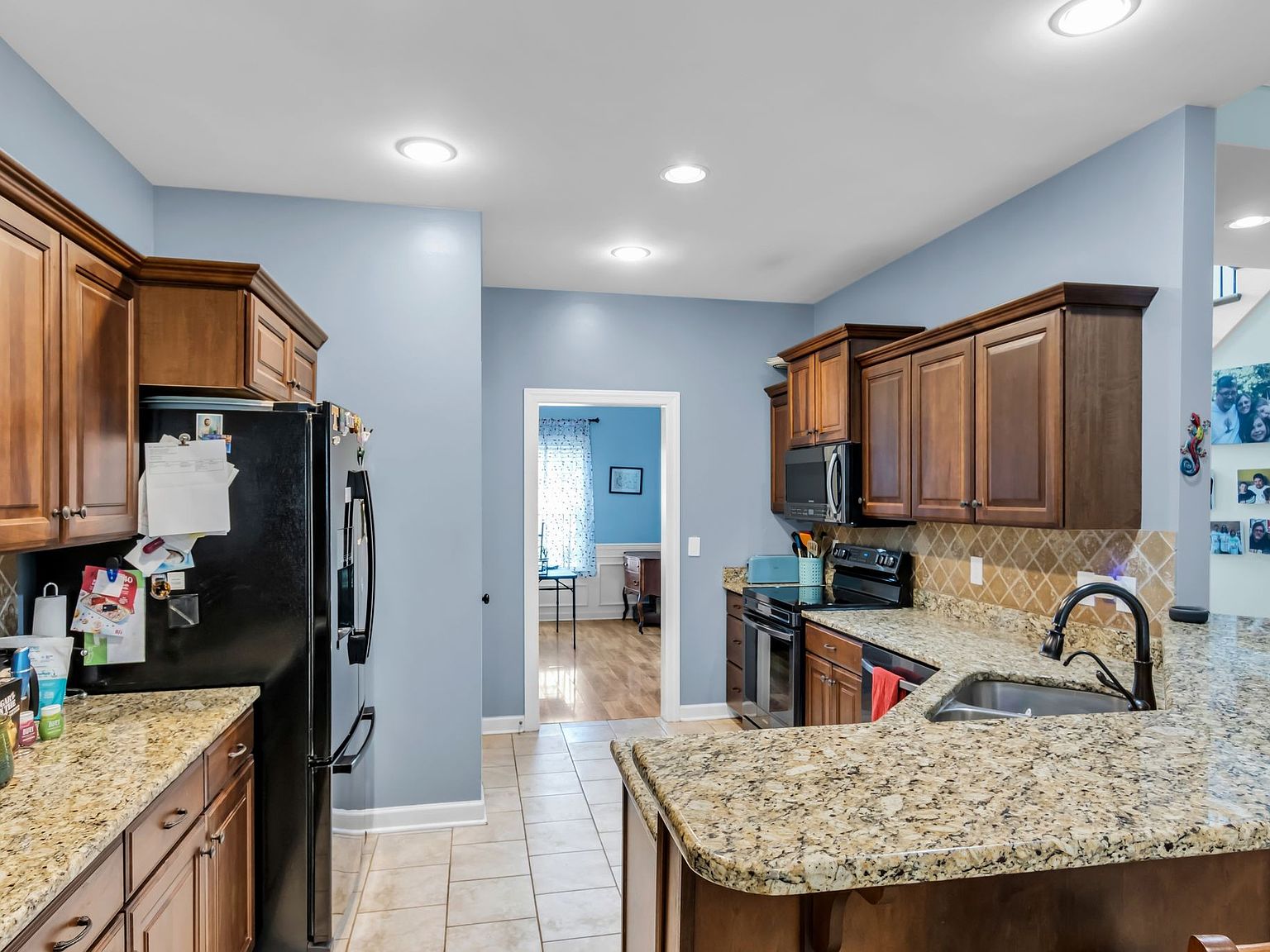 110 Bancroft Ct photo 10 Kitchen with blue walls, wooden cabinets, granite countertops, and a black side-by-side fridge; island and sink in foreground.