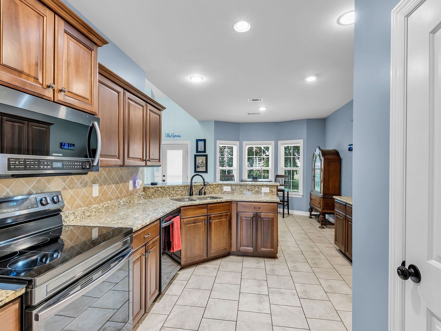 110 Bancroft Ct photo 11 Bright kitchen with warm wood cabinets, granite counters, stainless steel stove and microwave, and a breakfast bar by large windows.