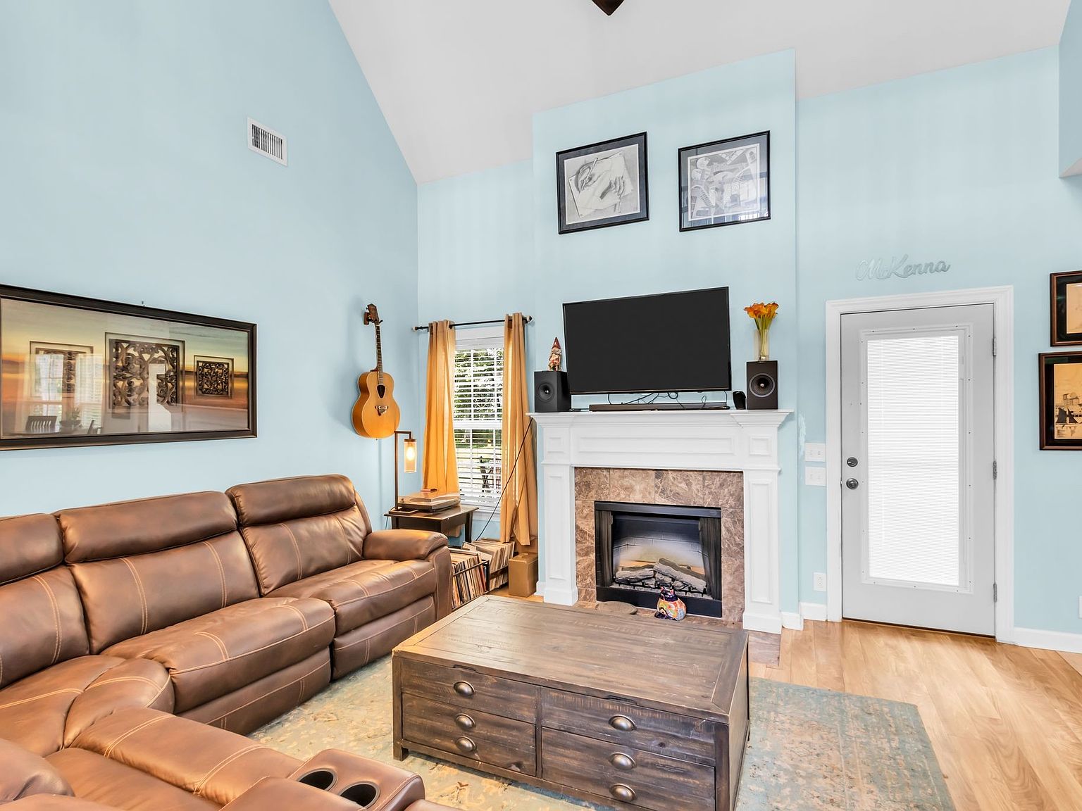 110 Bancroft Ct photo 17 Cozy living room with light blue walls, a brown leather sectional, and a white mantel fireplace topped by a flat-screen TV.