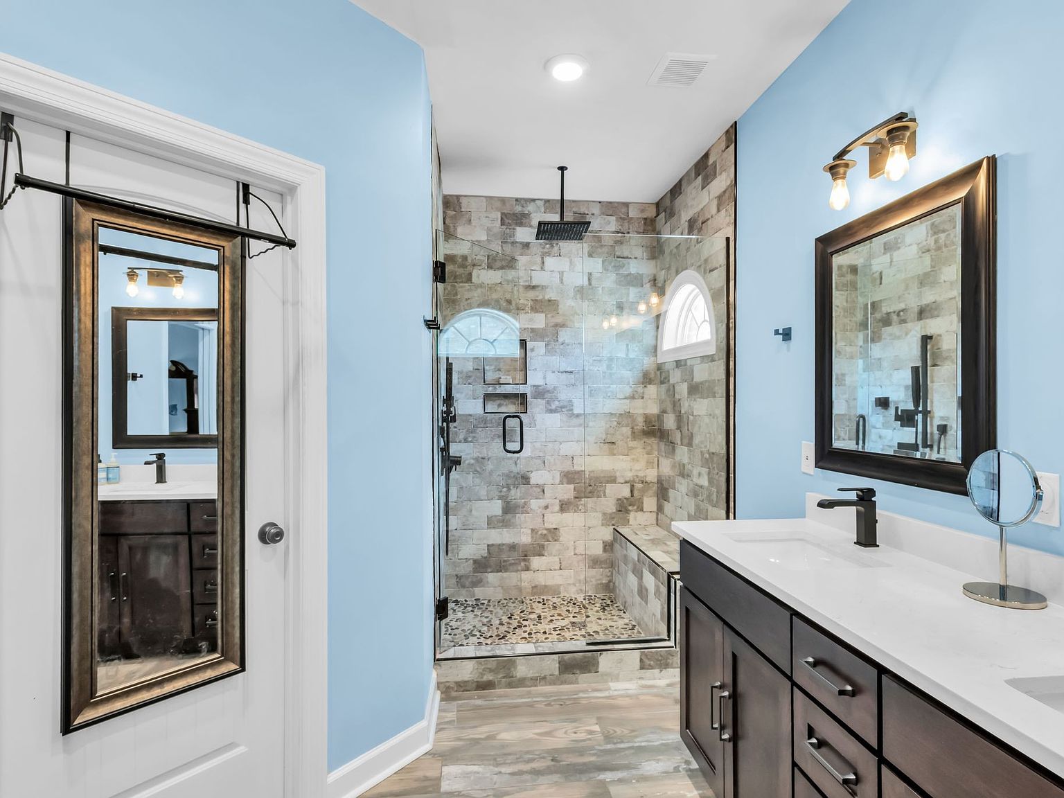 110 Bancroft Ct photo 21 Blue-wall bathroom with glass-enclosed shower, pebble floor, and dark wood vanity with white countertop and black faucet