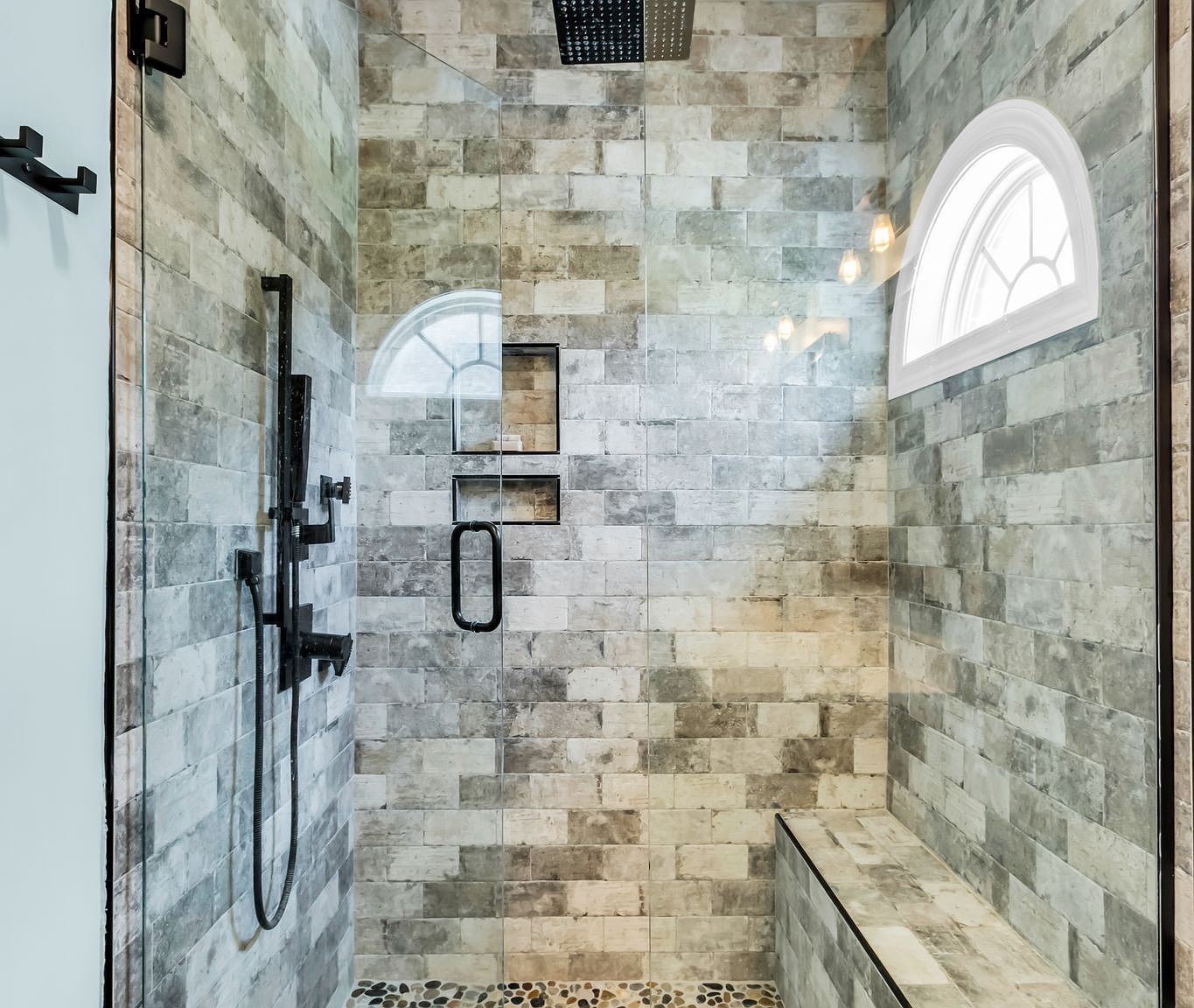 110 Bancroft Ct photo 22 Walk-in shower with gray stone tiles, a black rainfall head, handheld wand, glass door, and an arched window letting in light.