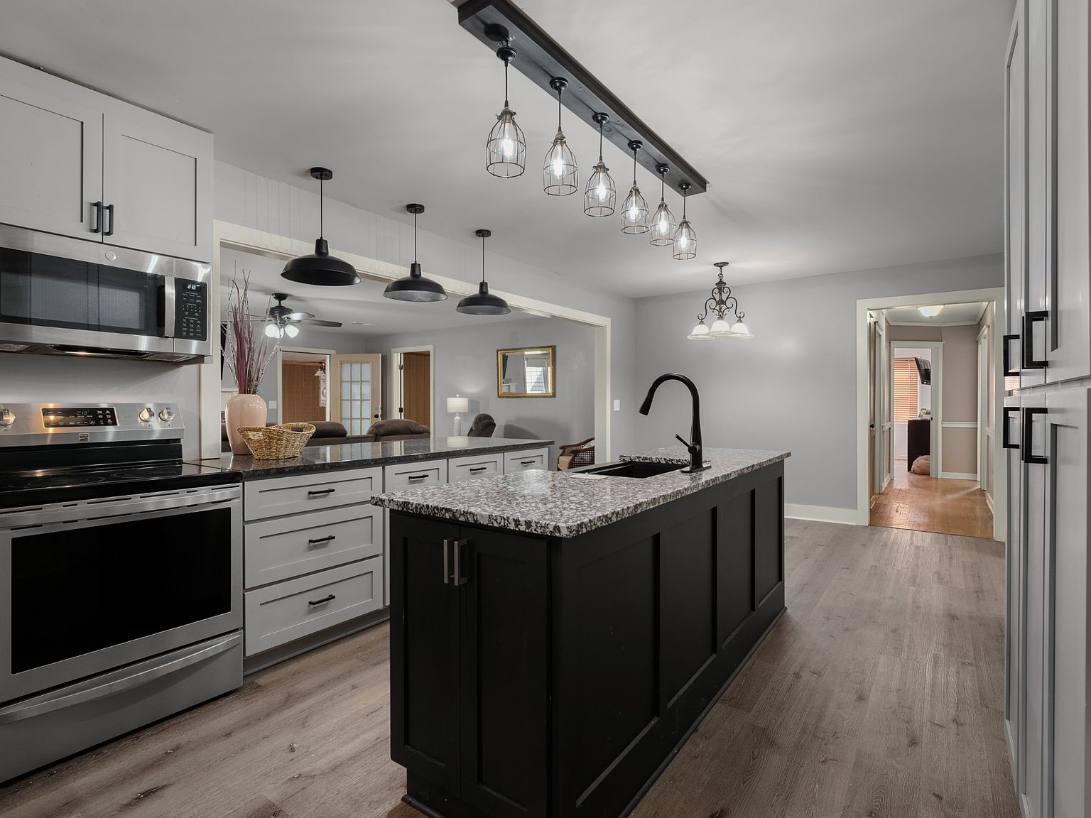 Open-concept kitchen with a black island, speckled granite countertop, and gray cabinetry under industrial pendant lights.