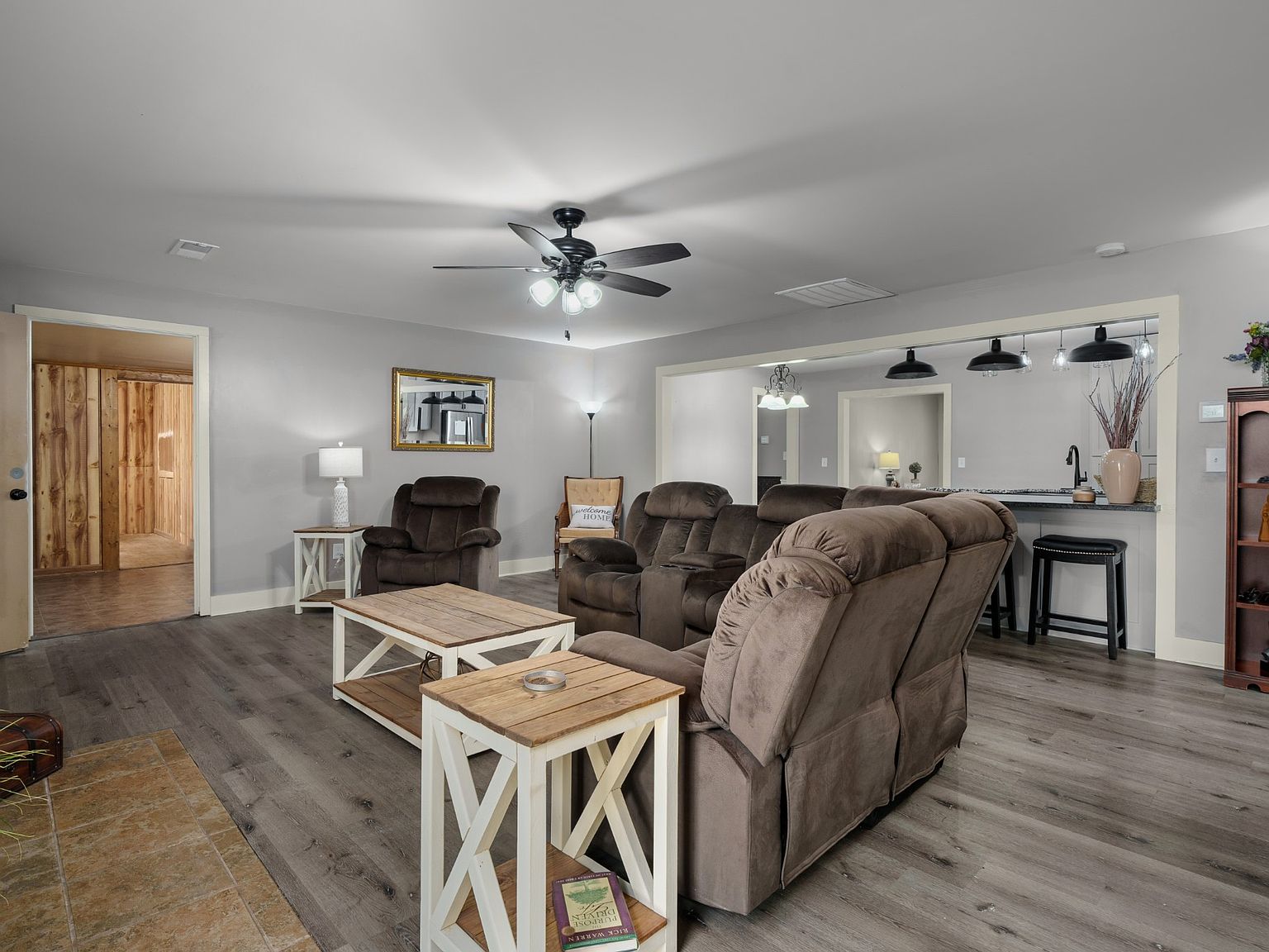 Cozy living room with brown reclining sofas, two white-and-wood coffee tables, and a ceiling fan in a gray-walled space.