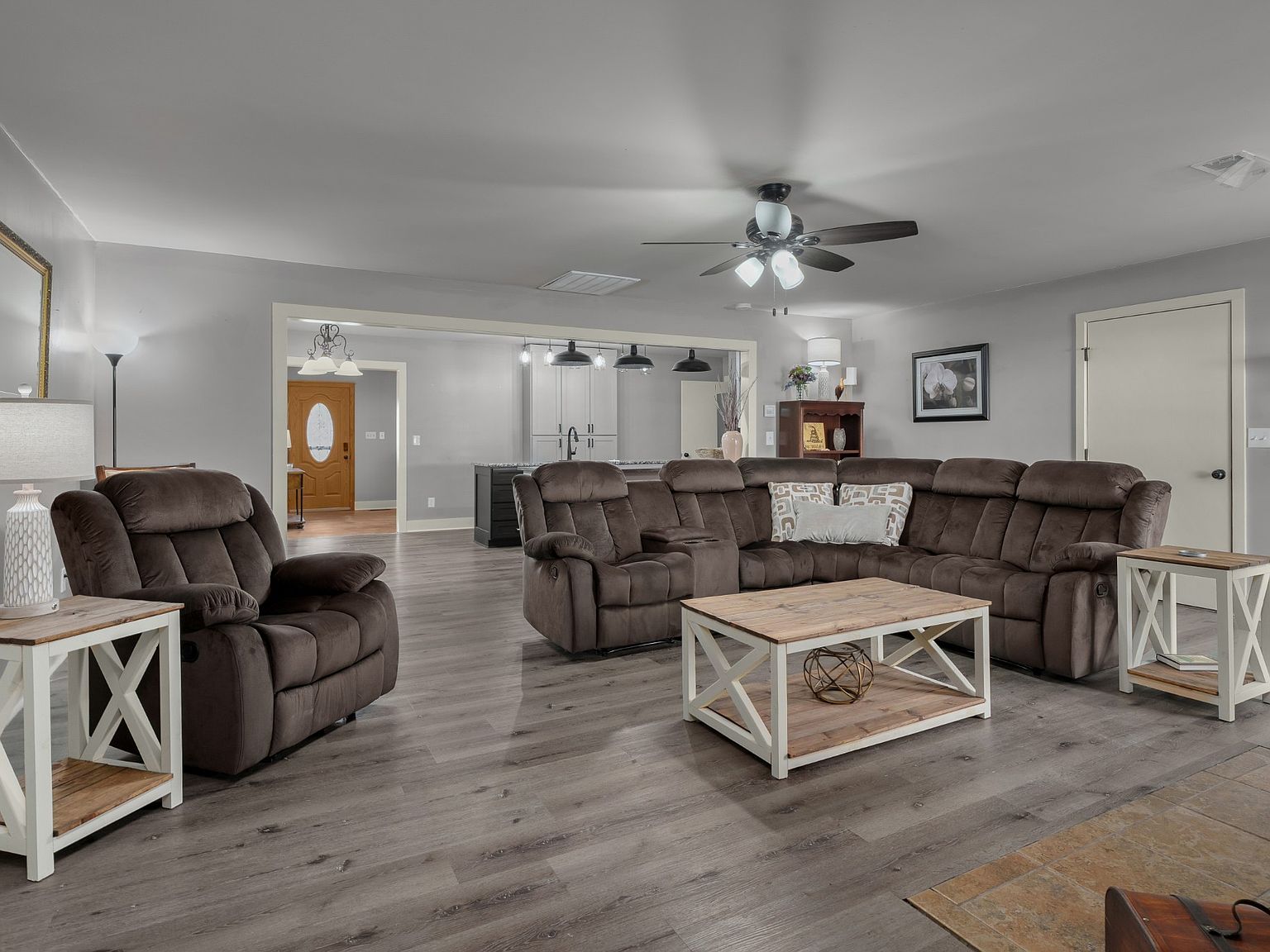 Open living room with a large brown sectional, two recliners, light wood coffee table, gray walls, and a ceiling fan with lights.