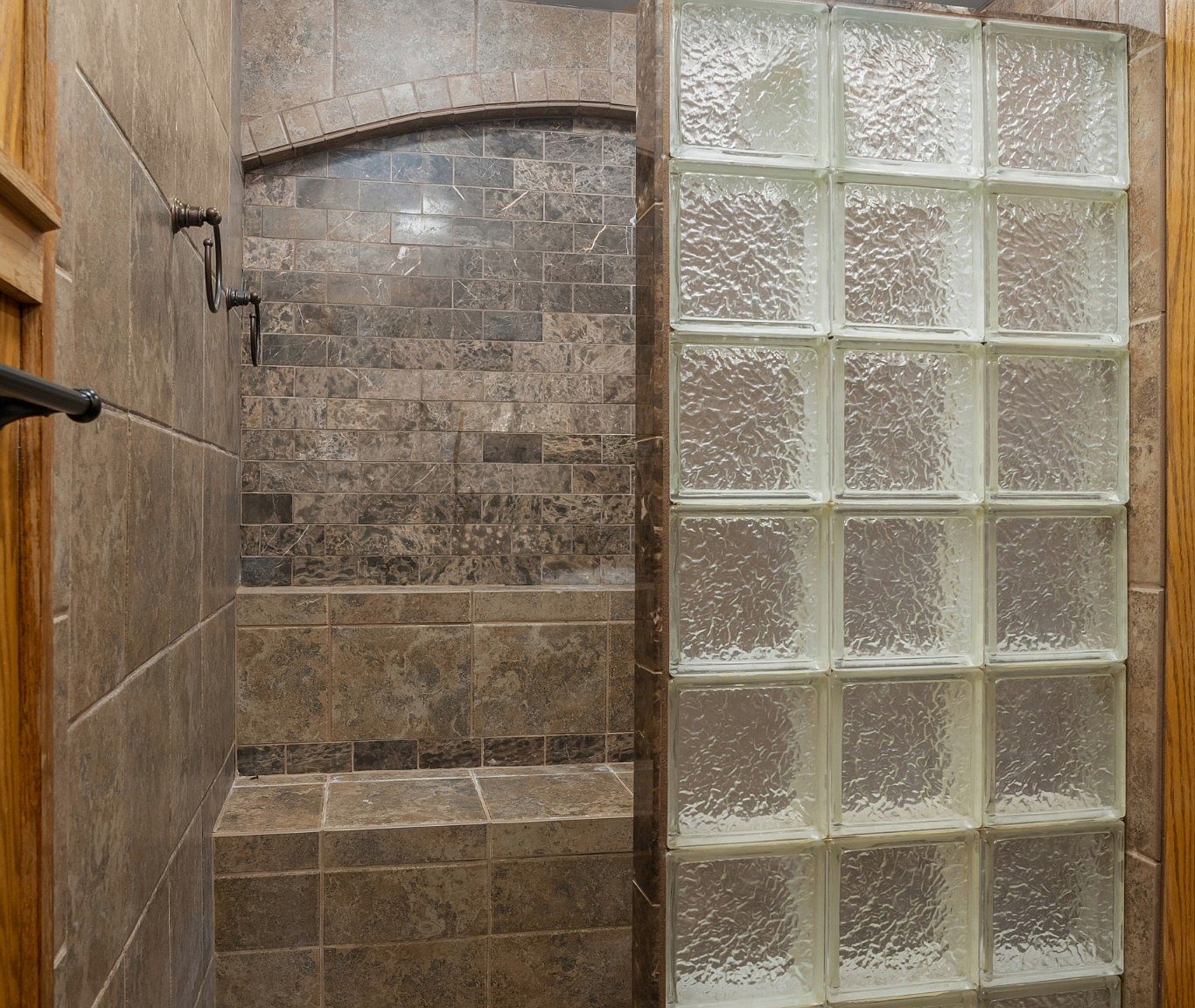 Dark tile-lined shower room with a built-in bench and an arched entry, and a glass block wall to the right