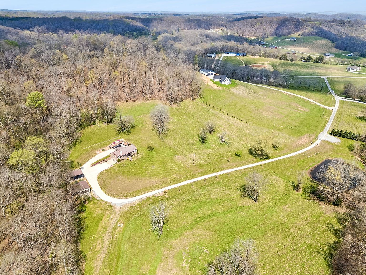 Aerial view of a rural property with a curved driveway, a house, and surrounding fields and woods,