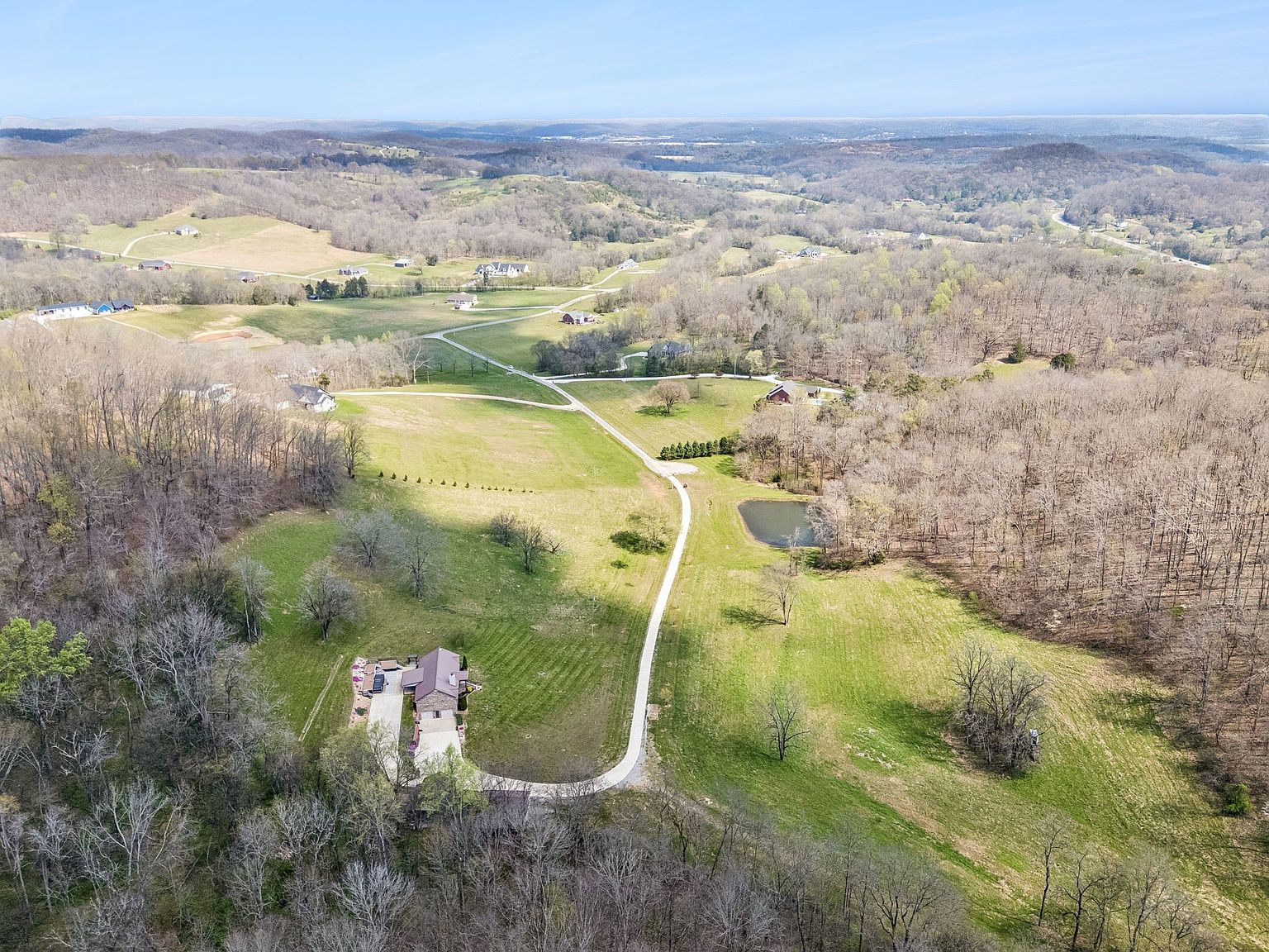 Aerial view of a rural landscape with winding roads, scattered houses, and leafless trees in early spring, under a blue sky.