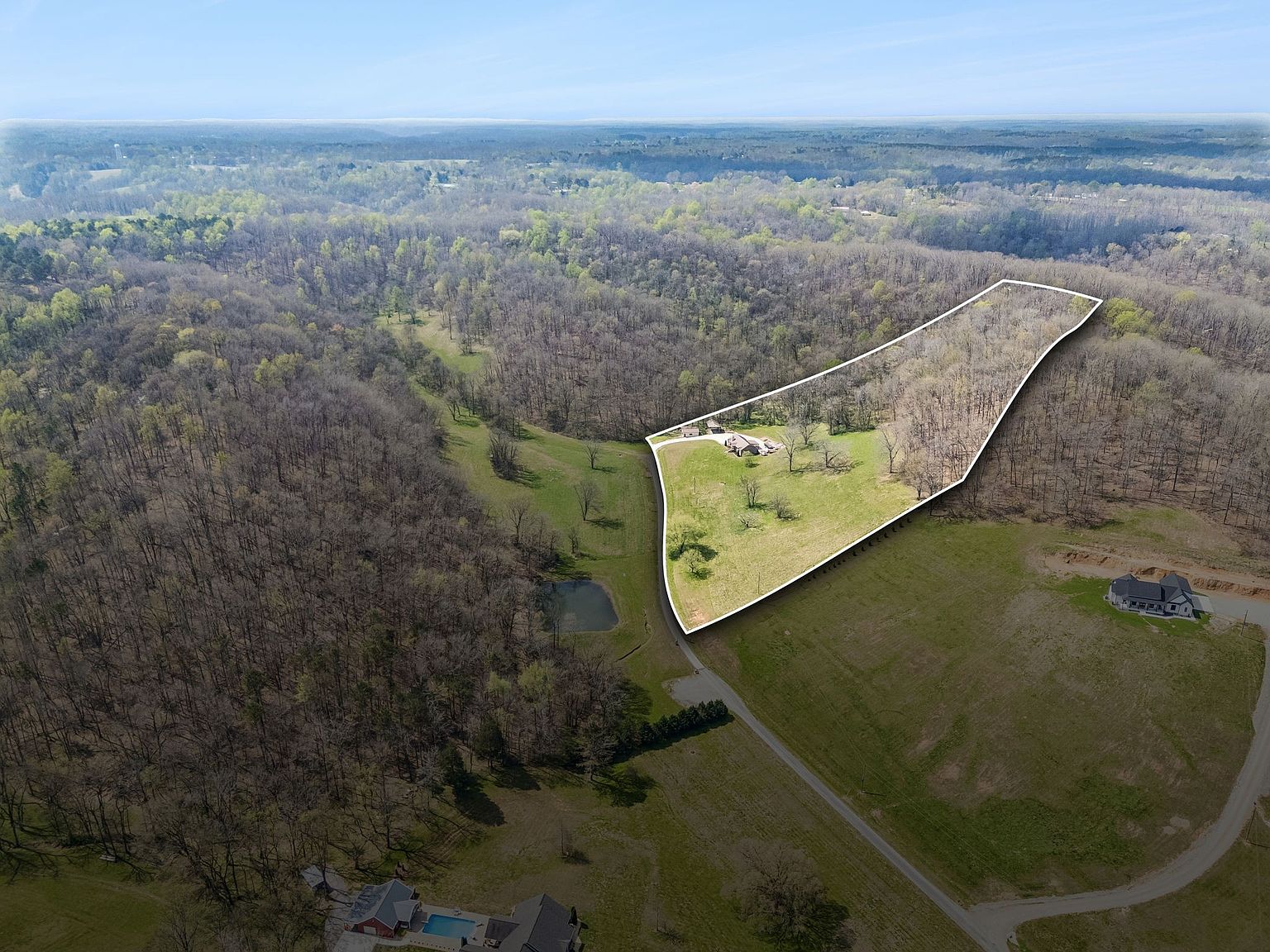 Aerial view of a large residential lot outlined in white, with a house near the front and dense trees surrounding the property.