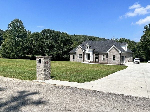 765 Scenic Cir photo 7 Front view of a single-story brick house with a long concrete driveway and a grassy lawn; a mailbox sits near the street and a white car is parked by the garage.