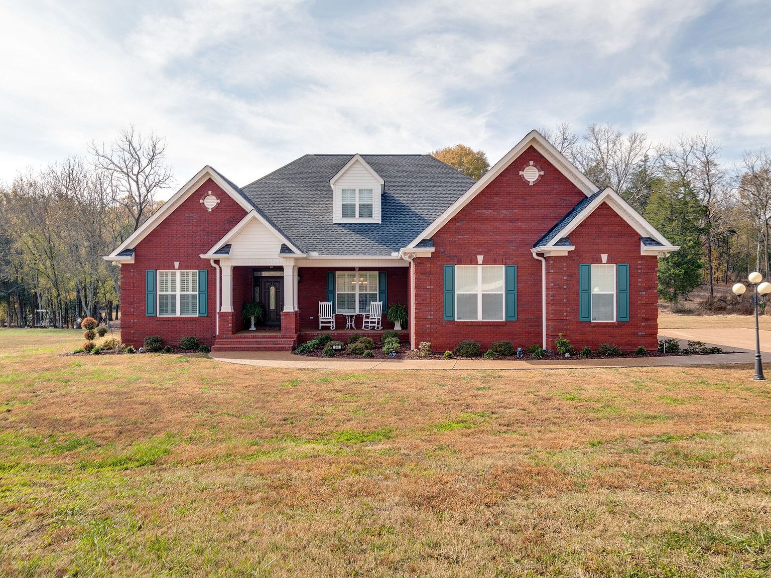 765 Scenic Cir photo 8 Brick ranch-style home with a central front porch, two gabled wings, teal shutters, and a neatly landscaped front yard under a blue sky.